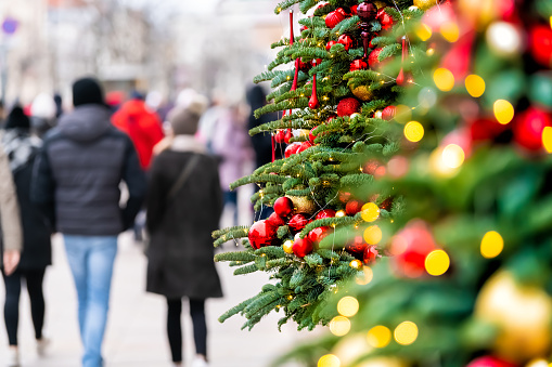 Side view of New Year Christmas tree with bokeh circles from lights illuminations and ornaments outside outdoors in Warsaw, Poland with people walking on street