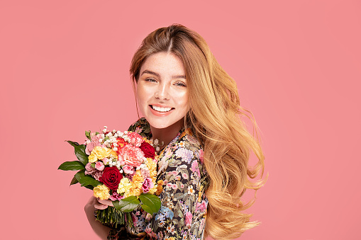 Beauty smiling woman with flowers in hand. Happy beautiful girl on pink pastel studio background. Spring fashion photo.