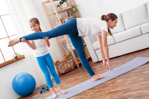 istock Healthy Lifestyle. Daugher helping mother holding her leg while she bending down stretching on yoga mat at home smiling happy 1221083350
