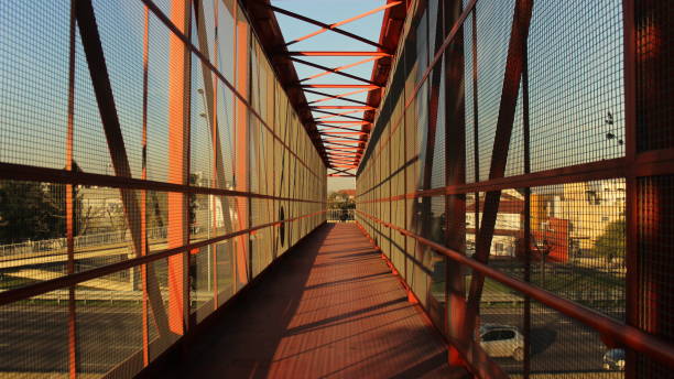 istock Pedestrian red metal bridge over a multi-lane highway, illuminated by the sunset orange light 1221090978