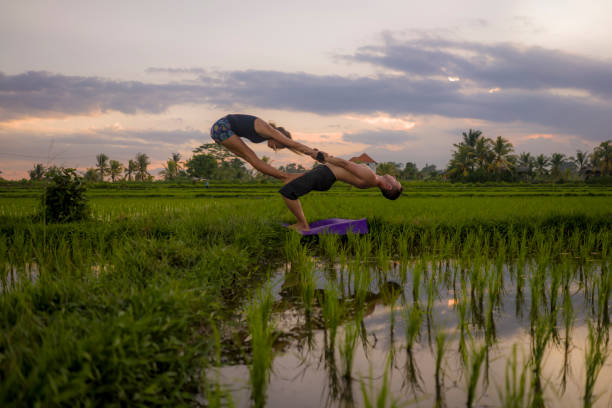 outdoors sunset acroyoga workout silhouette- young happy and fit couple practicing acro yoga drill at beautiful rice field enjoying nature and healthy lifestyle doing acrobatic pose outdoors sunset acroyoga workout silhouette- young happy and fit couple practicing acro yoga drill at beautiful rice field enjoying nature and healthy lifestyle doing acrobatic pose acroyoga stock pictures, royalty-free photos & images