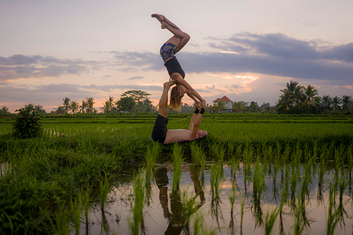 outdoors sunset acroyoga workout silhouette- young happy and fit couple practicing acro yoga drill at beautiful rice field enjoying nature and healthy lifestyle doing acrobatic pose