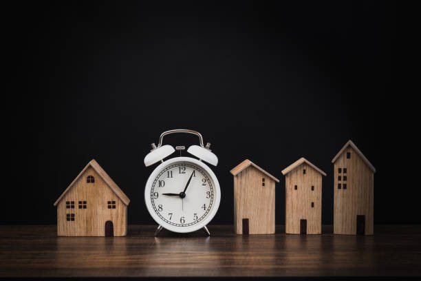 alarm clock with small house on wood and black background, real estate and time to get and buy property, resident and home stock photo
