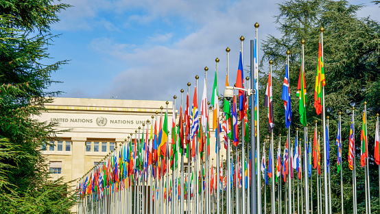 Geneva, Switzerland - November 8, 2019: color image depicting the exterior architecture of the United Nations (UN) building in the city of Geneva, Switzerland. The front of the building is lined with many flags and flagpoles, representing all the member nations of the UN