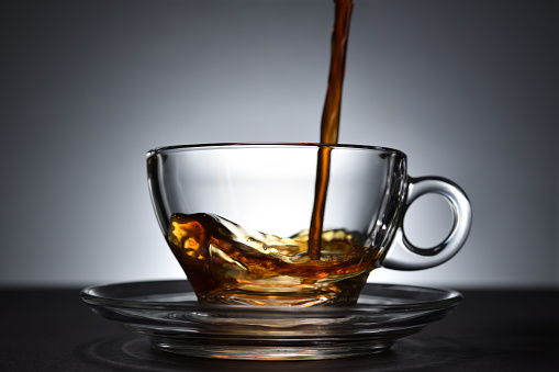 Pouring coffee on a transparent cup on black background