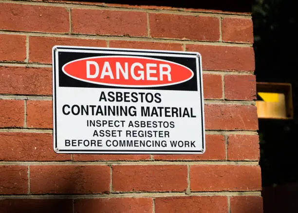 Close up photo of an industrial sign on a brick wall warning of asbestos