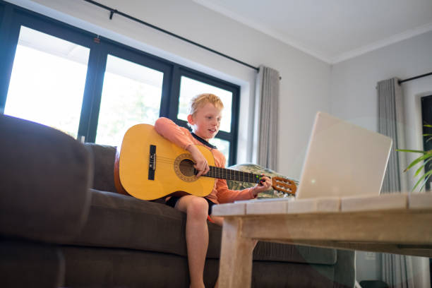 istock Boy enjoys practicing his guitar via teleconference with his music teacher 1221118390