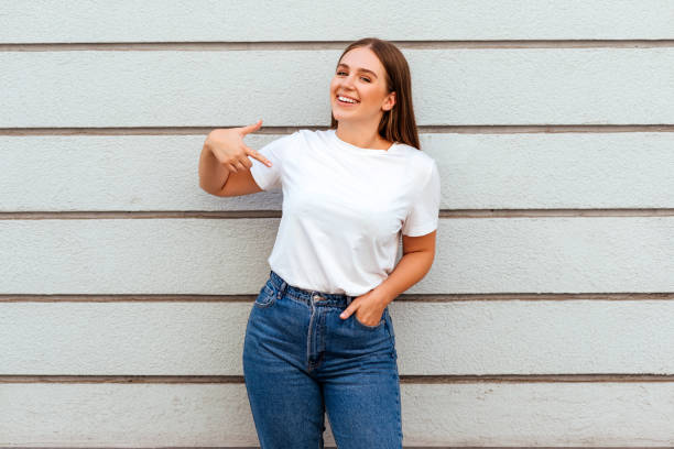 chica con una camiseta blanca de pie sobre un fondo de pared gris - t shirt child white portrait fotografías e imágenes de stock