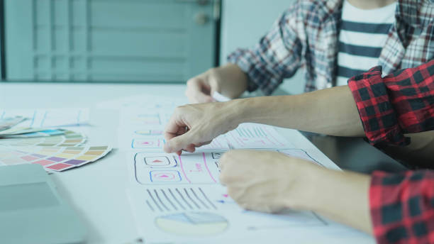 istock Designers man drawing ui/ux designers working and designing user interface for website and application, working together with partner planning and brainstorming sketch designs with computer laptop. 1221120706