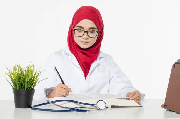 young female doctor with hijab sitting and writing something in her book over white background - Peluang Kerjaya Farmasi: Permohonan Diploma Farmasi di Widad