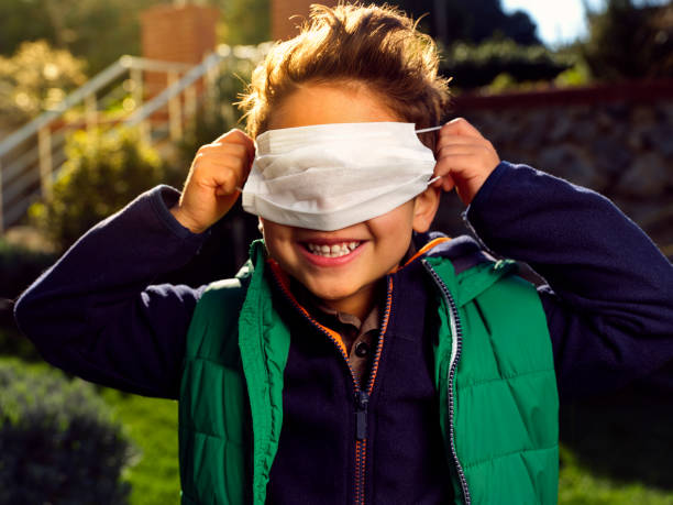 portret chłopca bawiącego się maską chirurgiczną w ogrodzie. - ciuciubabka zdjęcia i obrazy z banku zdjęć