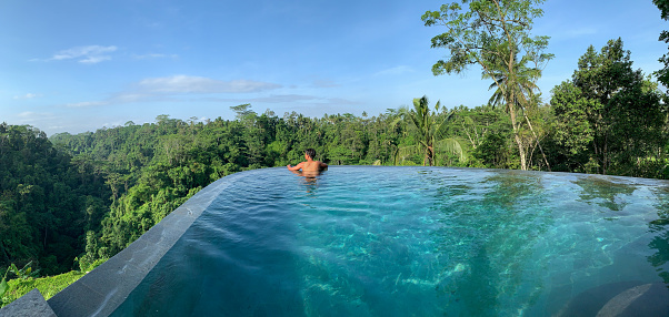 Young man naked sunbathing and relaxing in infinity private swimming pool at luxurious resort with a jungle view in rain forest,Ubud , Bali , Indonesia. panorama shot