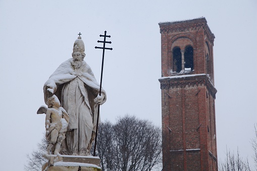 Statue of San Silvestro covered in the snow of a snowfall and the remains of the bell tower of San Domenico in the distance in central Mantova, Italy