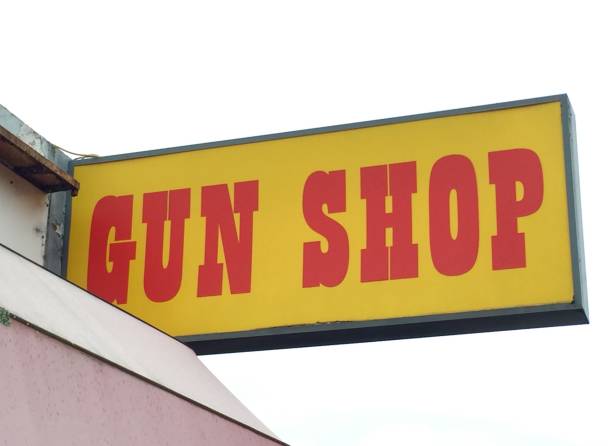Yellow and red gun store sign above a shop against a white sky stock photo