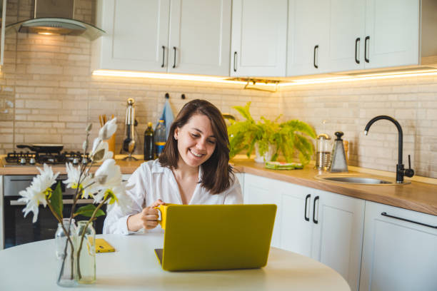 istock woman drinking tea from yellow mug working on laptop. kitchen on background 1221125221