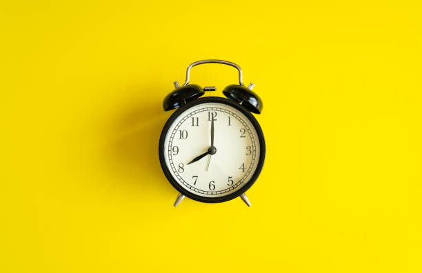 istock black alarm clock from 7 a.m. to 8 a.m. with bright yellow  background and shadows from the changing light of the sun's movements in morning and working hours concept front shot. 1221127541