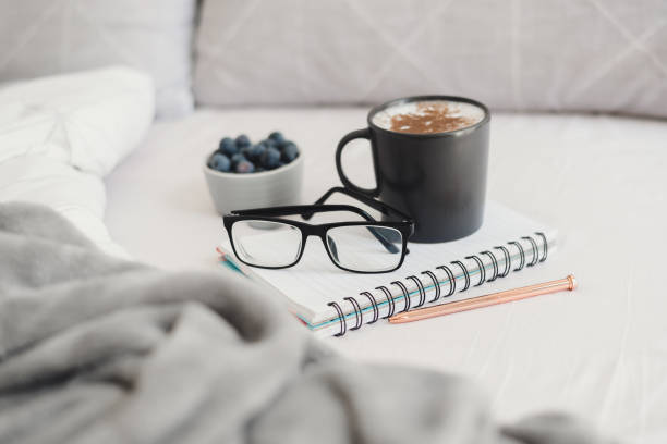 istock Cappuccino coffee with cinnamon and blueberries served in bed with reading glasses, note book and pen for working or studying from bed. Breakfast in bed 1221127564