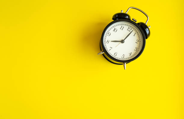 istock black alarm clock from 7 a.m. to 8 a.m. with bright yellow  background and shadows from the changing light of the sun's movements in morning and working hours concept front shot. 1221127575