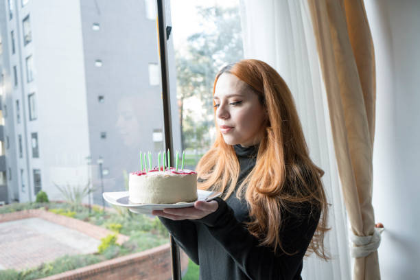 istock Woman with her birthday cake looking out the window while being quarantined 1221128375