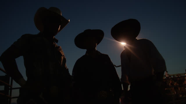 Pushing In Shot of Three Men in Silhouette Wearing Cowboy Hats at a Competitive Bull Riding Event at Night