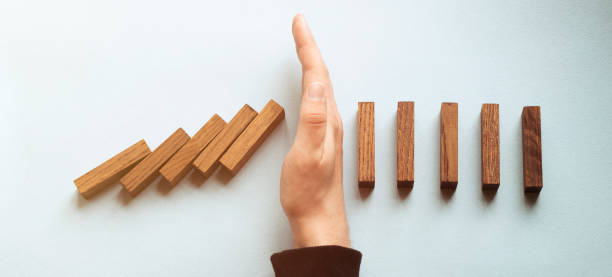Wide view image of male hand stopping falling dominos. Over blue background. stock photo