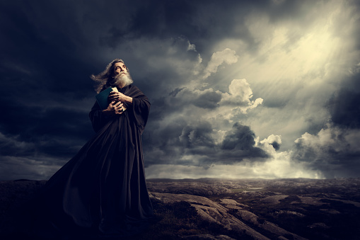 Monje sosteniendo la Biblia mirando hacia Dios cielo luz, viejo sacerdote en negro Robe en la tormenta photo