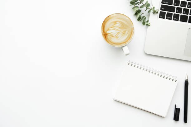 istock White minimalist office desk table with blank notebook page with pen, cup of latte coffee and laptop computer. Top view with copy space, flat lay. 1221135494