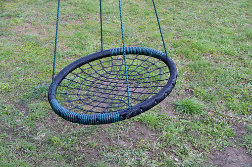 Black round rope web nest for swinging closeup on green grass field background outdoors in yard. Children outdoors leisure activities concept.