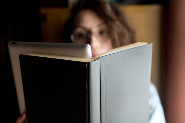 istock The girl is holding an open book in front of which a tablet is embedded 1221148027