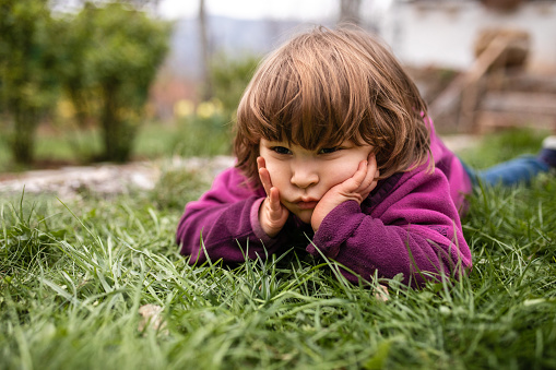 Borred little girl lying in grass alone in her back yard