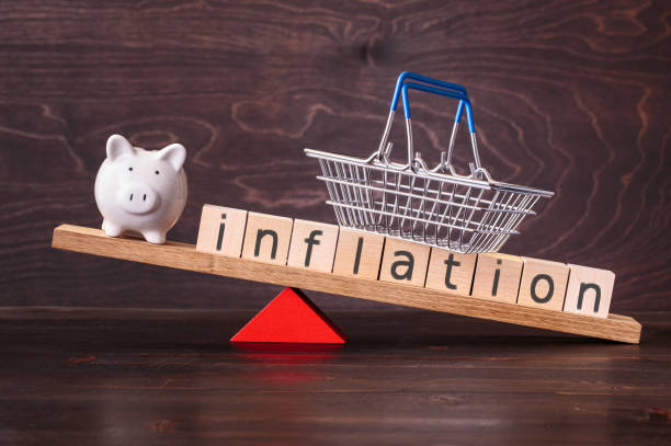 Inflation and piggy bank on seesaw Inflation spelled in letters with shopping basket and piggy bank on seesaw against dark background inflation stock pictures, royalty-free photos & images