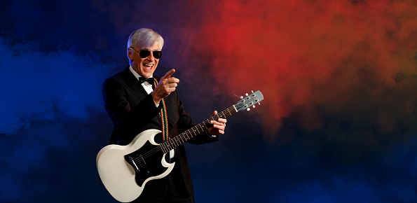 Musician Guitarist Active senior Handsome man playing guitar. Blue  background, with rays of light and special effects smoke.