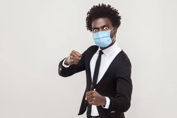 ¡no te acerques más! retrato de hombre enojado en traje negro con máscara médica quirúrgica de pie con puños de boxeo y listo para atacar o defensa. - serious punching fighting displeased fotografías e imágenes de stock