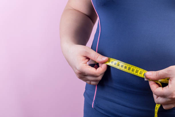 mujer con sobrepeso con cinta métrica en la cintura, primer plano - régimen alimenticio fotografías e imágenes de stock
