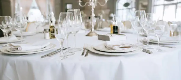 Photo of Elegant wedding white table set. Plates, forks and glasses