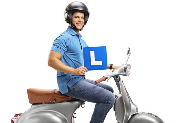 istock Young man on a silver vintage scooter wearing a helmet and holding a learner plate 1221163717