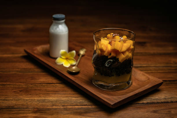 A cup of mango sticky rice on a wooden table. Thai dessert with coconut milk
