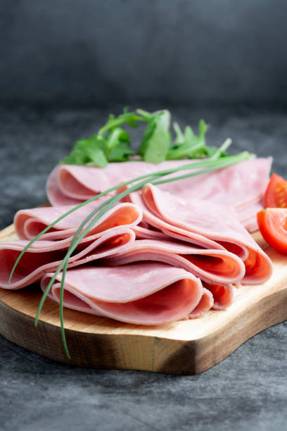 istock Close up ham slices isolated on cutting board over dark background. 1221164241