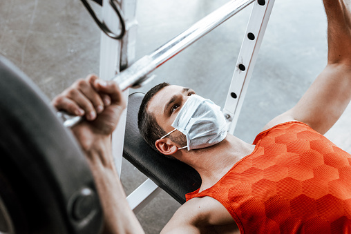 enfoque selectivo del deportista en la máscara médica haciendo ejercicio con barbell en el gimnasio photo