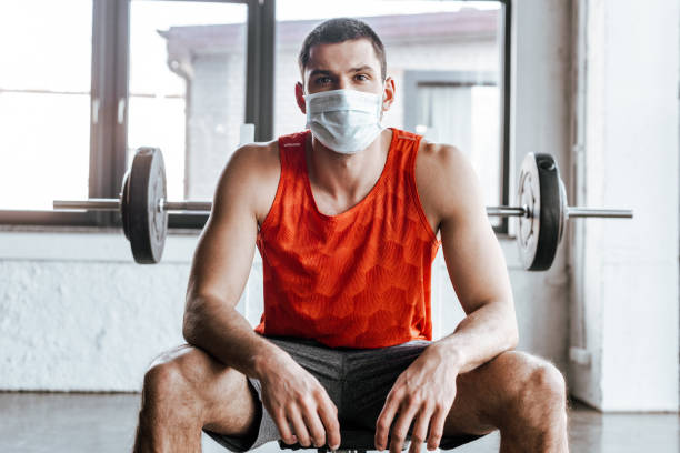 deportista atlético en máscara médica sentado cerca de barbell en el gimnasio - fotografía temas fotografías e imágenes de stock