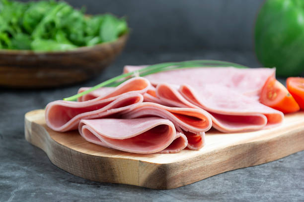 istock Close up ham slices isolated on cutting board over dark background. 1221164342