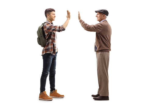 Full length profile shot of a male student greeting an elderly man with a high-five gesture isolated on white background