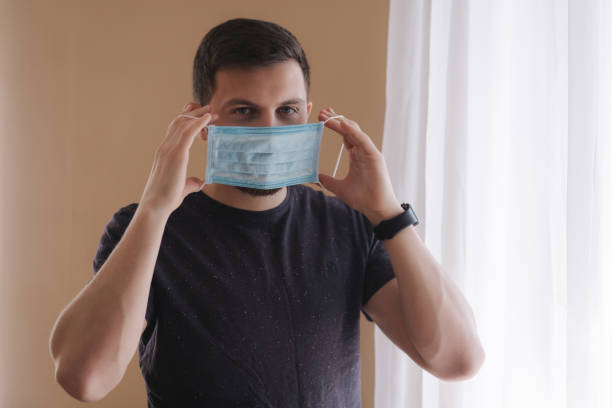 istock Man put on madical mask at home. Young man in protective mask. Coronavirus theme 1221170926