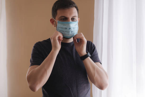 istock Man put on madical mask at home. Young man in protective mask. Coronavirus theme 1221170942