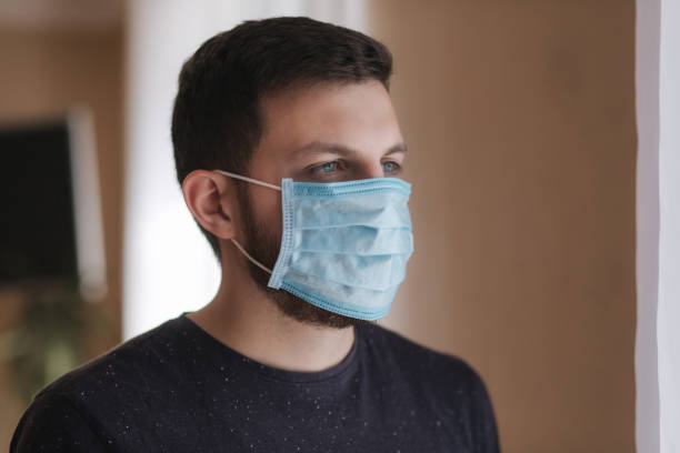 istock Man put on madical mask at home. Young man in protective mask. Coronavirus theme 1221170956