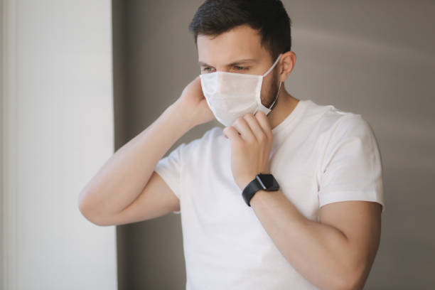 istock Young man put on protective mask and look s out the window. Alone at home in quarantine. Coronavirus theme. Stay at home 1221171732