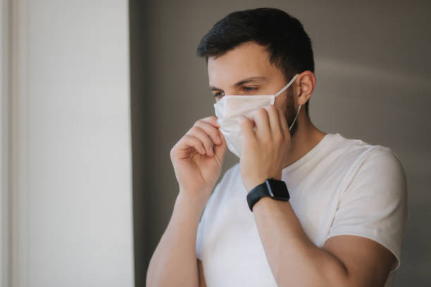 istock Young man put on protective mask and look s out the window. Alone at home in quarantine. Coronavirus theme. Stay at home 1221171743