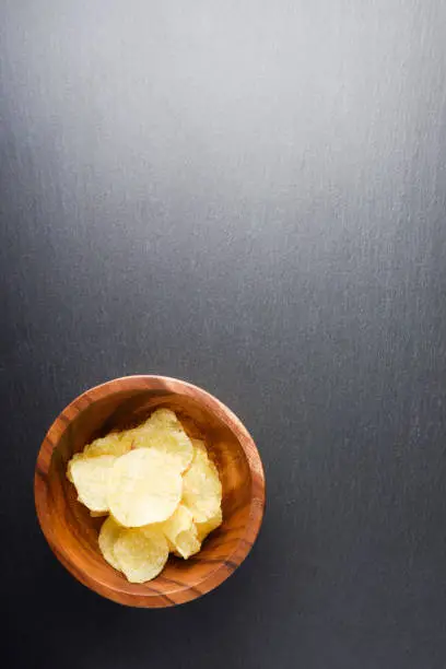 Crispy potato chips in woodenbowl on dark slate stone background