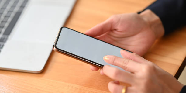 istock Closeup woman's hands holding and using a smartphone while sitting/relaxing at the wooden working desk over comfortable living room as background. 1221175837