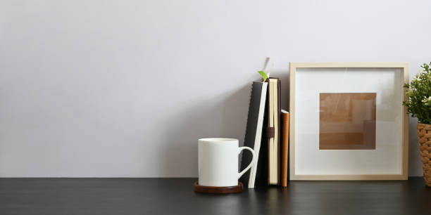 istock Working desk along with book, notebook, picture frame, potted plant and coffee cup putting together on it with white cement wall as background. Orderly workspace concept. 1221175877